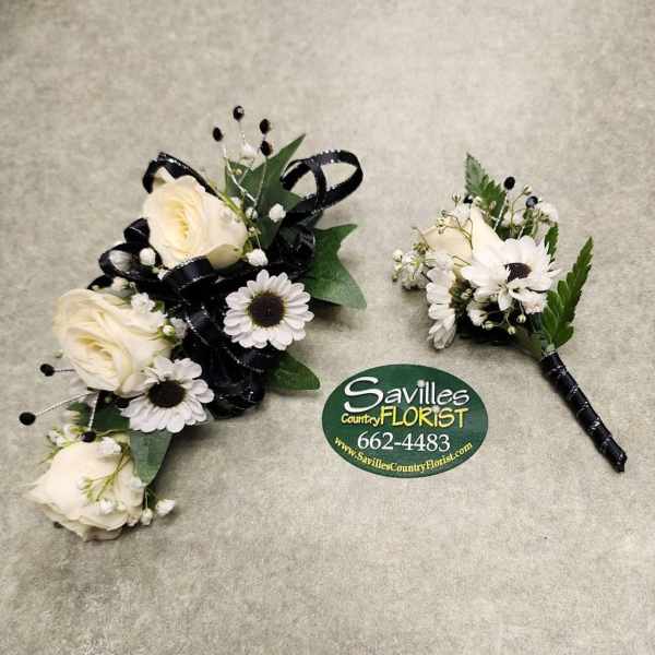 Two white floral boutonnieres with black ribbon accents on a gray surface