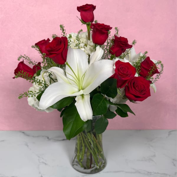Red roses and a white lily in a clear glass vase.