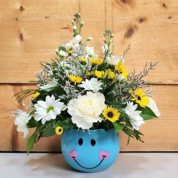 White and yellow flowers arranged in a blue smiley-face pot