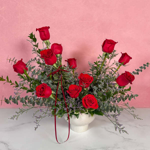 Arrangement of red roses in a white vase with trailing greenery