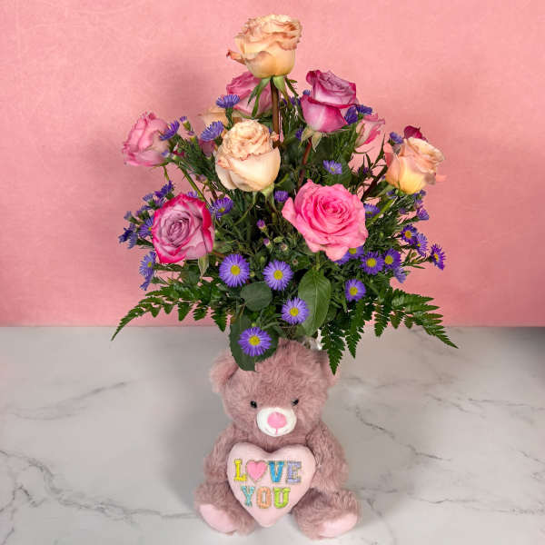 Pink and peach roses in a teddy bear vase with a plush bear holding a heart