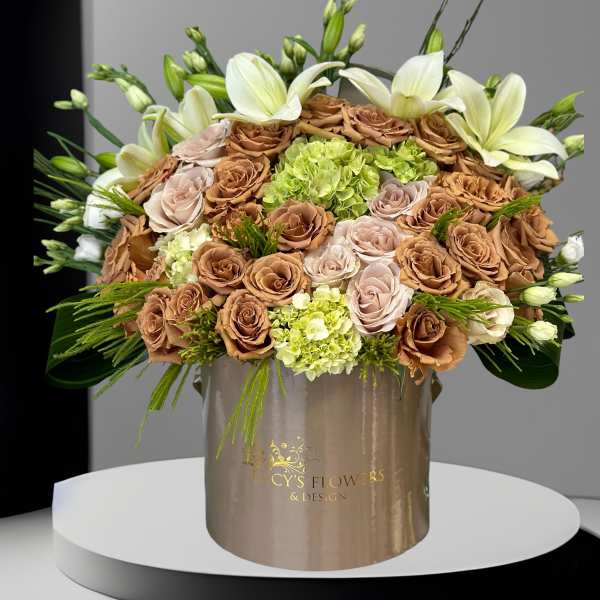 Large bouquet of tan and blush roses with white lilies in a gold box