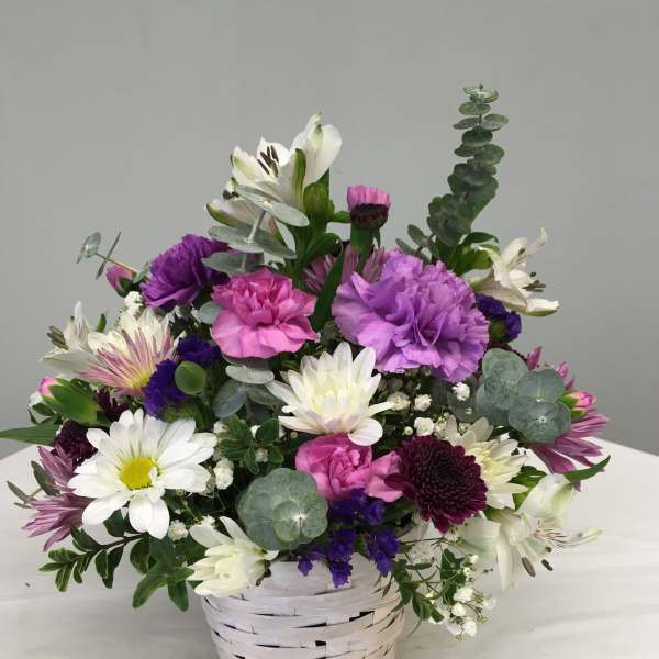 Mixed bouquet of white, pink, and purple flowers in a white basket