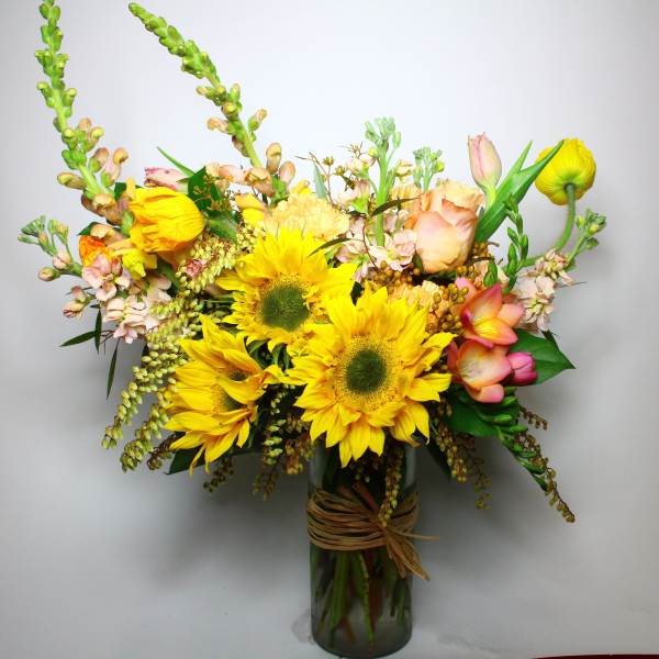 Bouquet of yellow sunflowers and pastel flowers in a glass vase