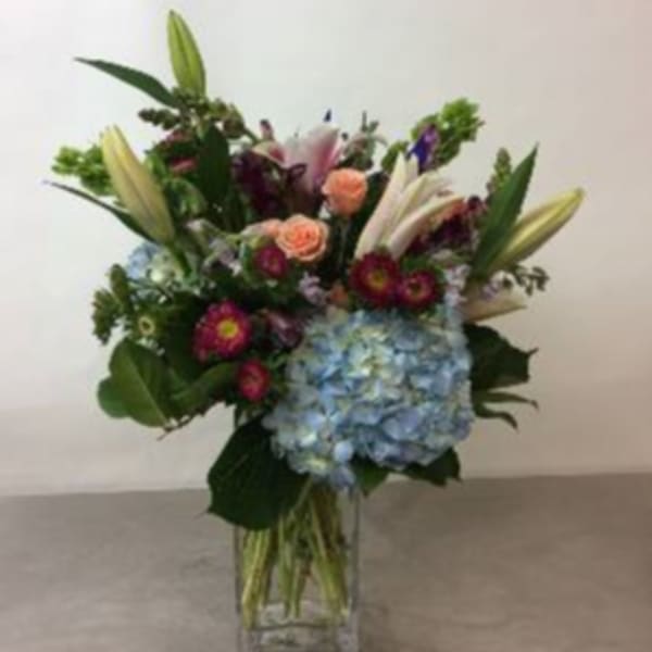 Mixed bouquet with lilies, roses, and blue hydrangea in a clear vase