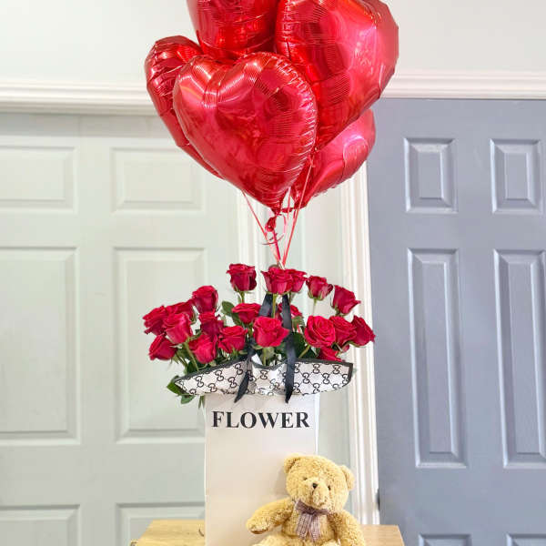 Red roses in a gift box with heart-shaped balloons and a teddy bear