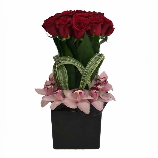 Red roses arranged in a black square vase with pink orchids at the base