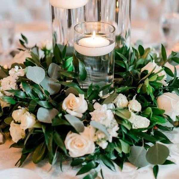 Three glass candle holders surrounded by white roses and greenery