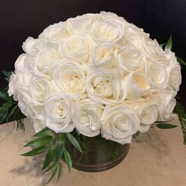 White rose bouquet in a low glass vase with green foliage
