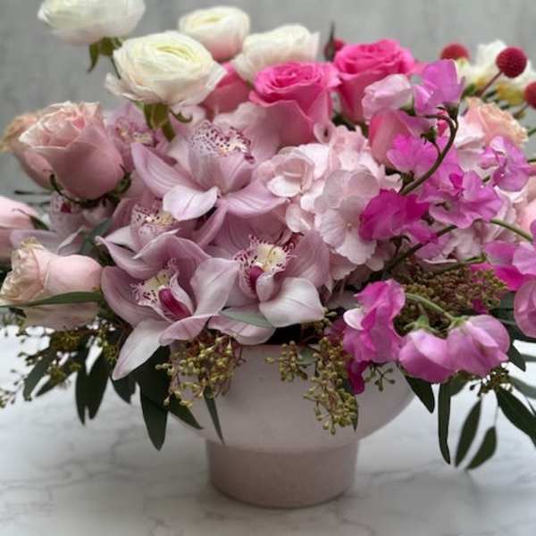 Low pink and white arrangement with roses, orchids, ranunculus and hydrangeas in a blush ceramic bowl