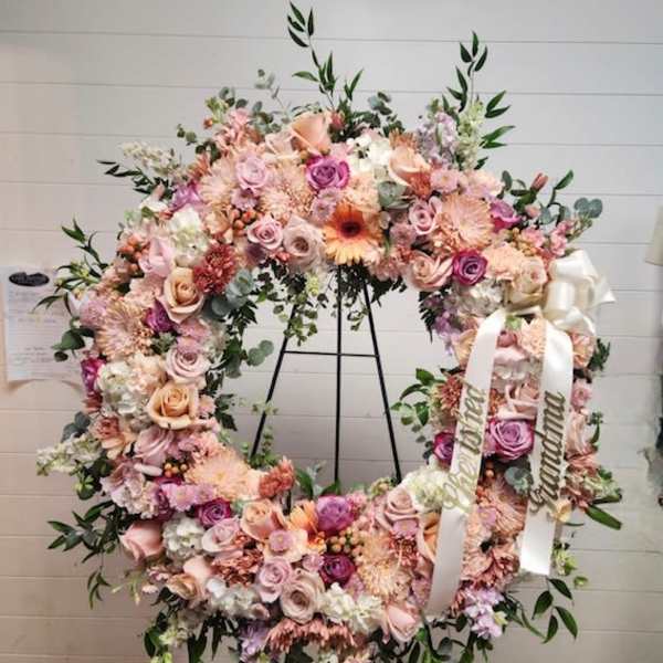 Large pastel floral wreath on a black stand with white ribbons