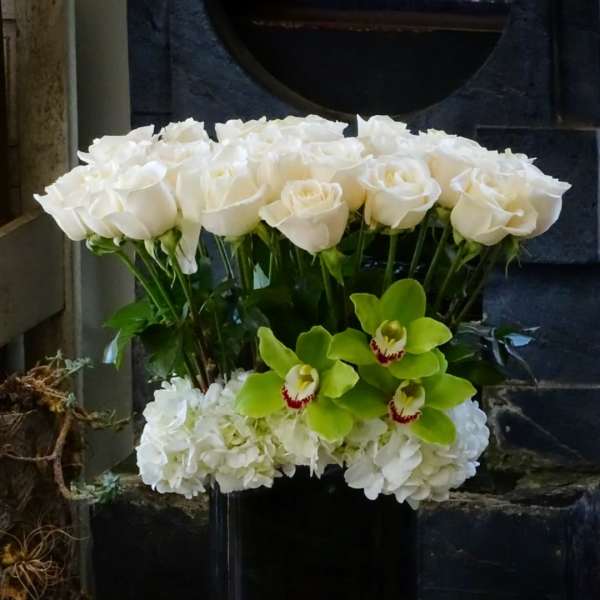 White roses and green orchids in a black vase