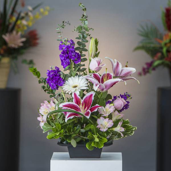 Mixed bouquet with pink lilies, white gerbera daisies, and purple blooms in a black container