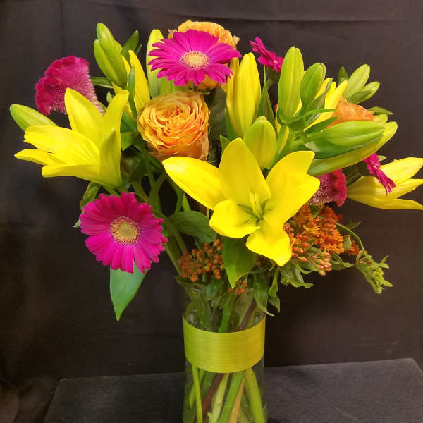 Bouquet of yellow lilies, pink gerbera daisies, and orange roses in a glass vase