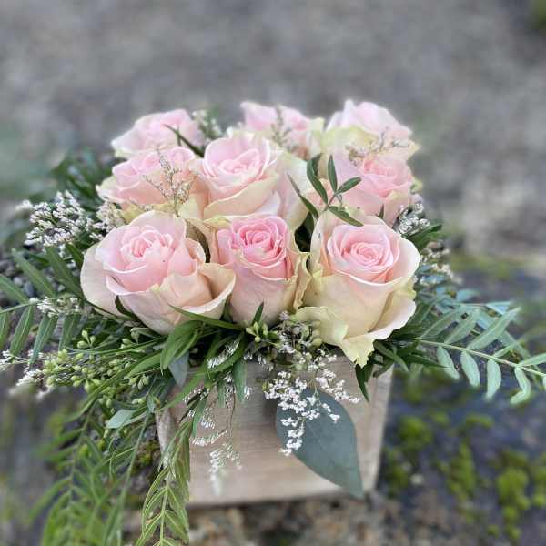 Pink roses arranged in a low wooden box with greenery