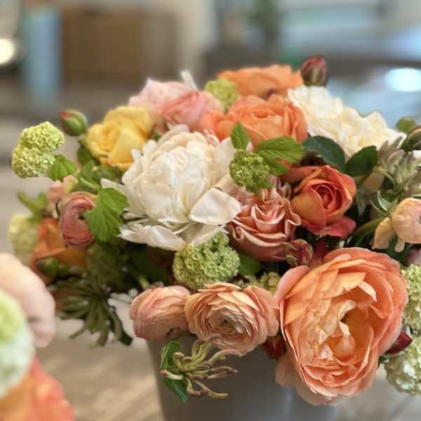 Mixed bouquet of peach, white, and yellow flowers in a gray vase