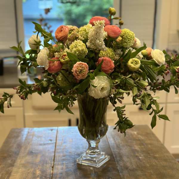 Mixed bouquet of coral, white, and green flowers in a clear glass vase