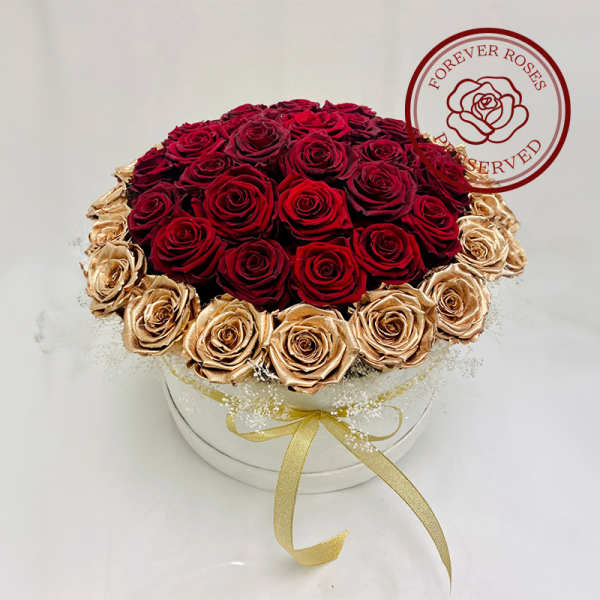 Round box arrangement of red and gold preserved roses with a ribbon bow