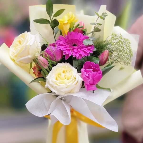 Bouquet of pink and white flowers wrapped in cream paper with a yellow ribbon