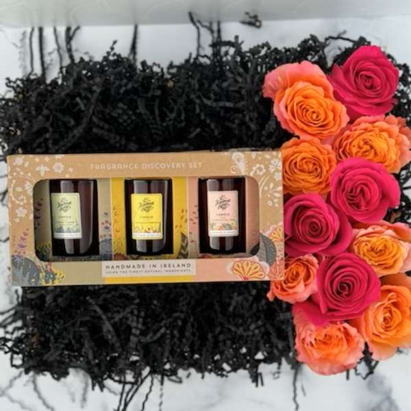 Boxed candle gift set on black shred with a row of pink and orange roses on the side