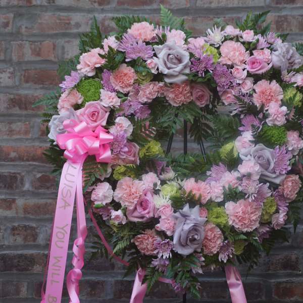 Heart-shaped floral wreath with pink and lavender flowers on a brick wall