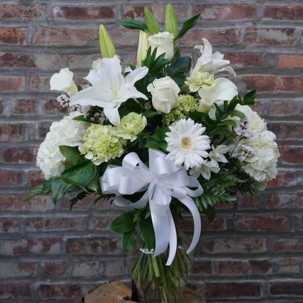 White floral arrangement with lilies, roses, and a ribbon bow