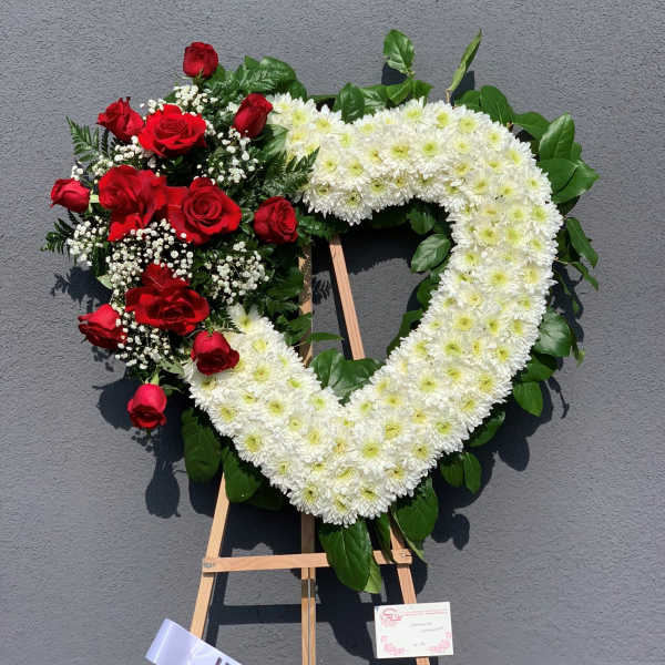 Heart-shaped floral wreath with red roses and white chrysanthemums on an easel