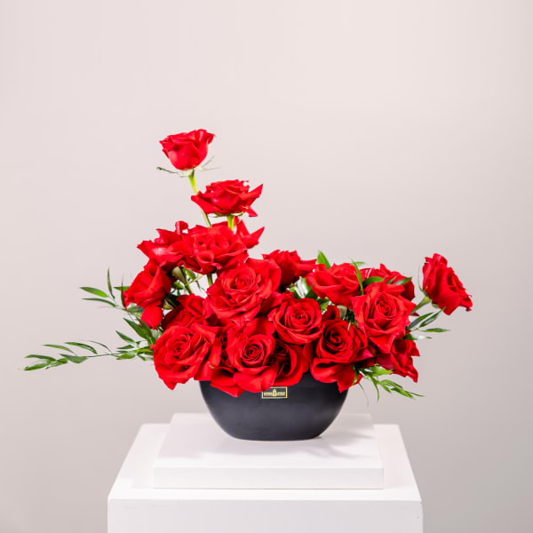 Red roses arranged in a black vase on a white pedestal
