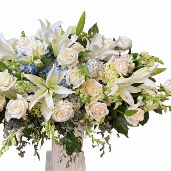 Large white floral arrangement with lilies and roses in a tall vase