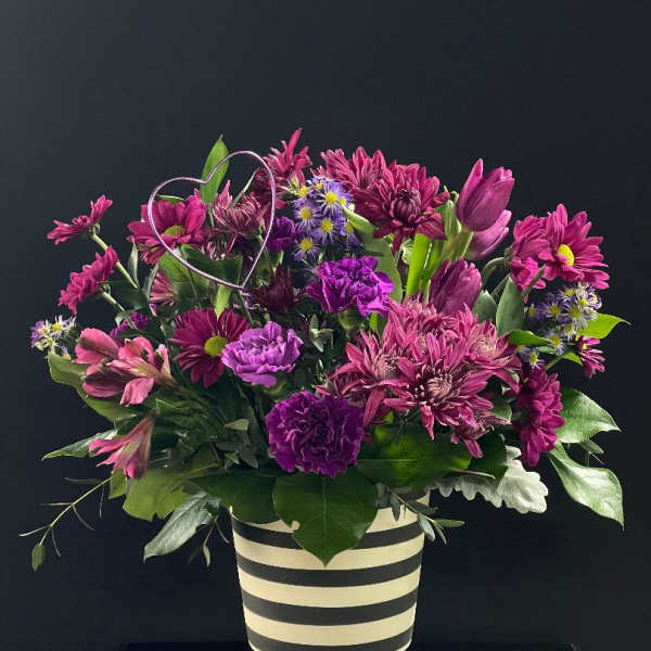 Purple and pink mixed bouquet in a striped vase with a wire heart accent