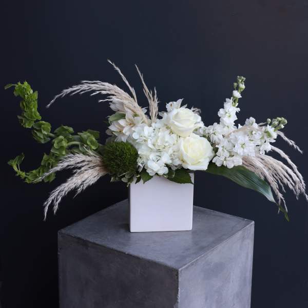 White floral arrangement in a square vase with feathery grasses