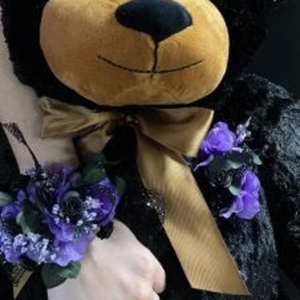 Black teddy bear with purple floral accents and a gold ribbon bow