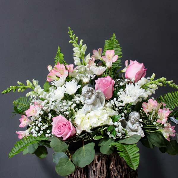 Pink and white floral arrangement with angel figurines in a vase
