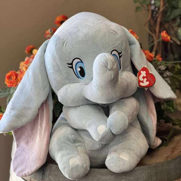 Plush gray elephant toy sitting in a wooden barrel with orange flowers behind it