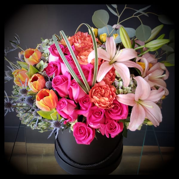 Bright mixed bouquet of pink roses, lilies, and orange tulips in a black hatbox