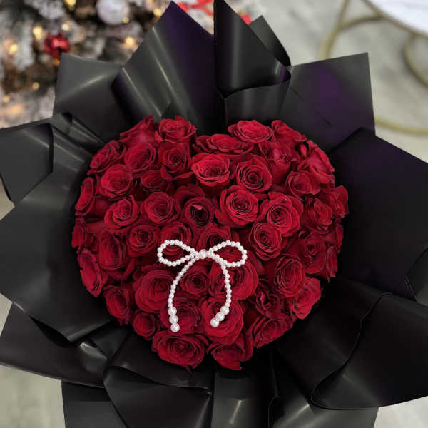 Heart-shaped bouquet of red roses with a pearl bow on black wrap