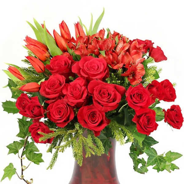 Arrangement of red roses, tulips, and alstroemeria in a red glass vase with trailing ivy.