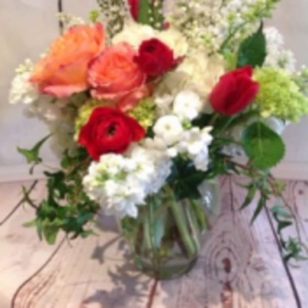 Mixed arrangement of peach roses, red blooms, and white flowers in a clear glass vase