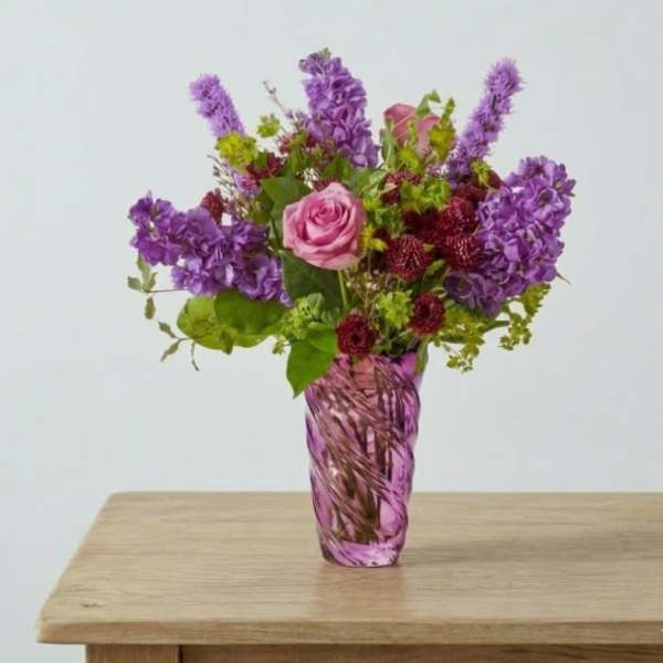 Pink and purple flower arrangement in a purple glass vase