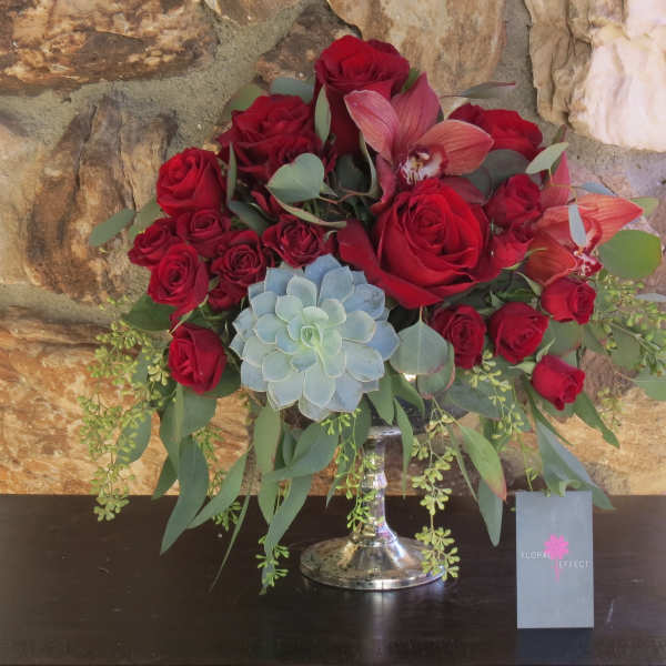Red roses and orchids arranged in a silver vase with a blue succulent accent