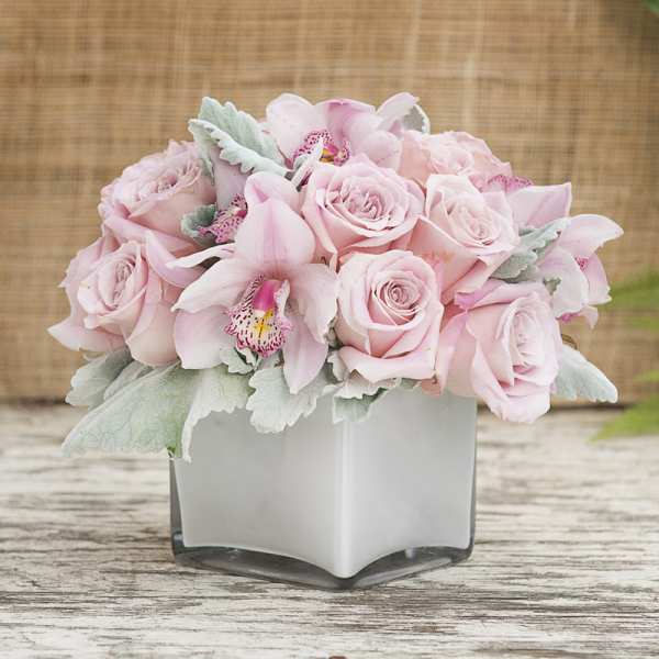 Pink roses and orchids arranged in a white square vase