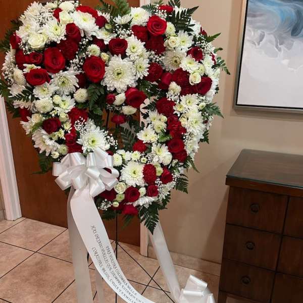 Heart-shaped standing wreath of red and white flowers with a white ribbon