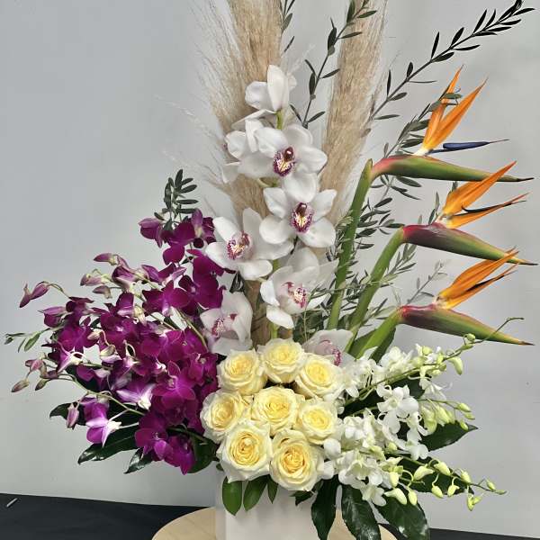 Tropical arrangement with orchids, roses, and bird of paradise in a white vase