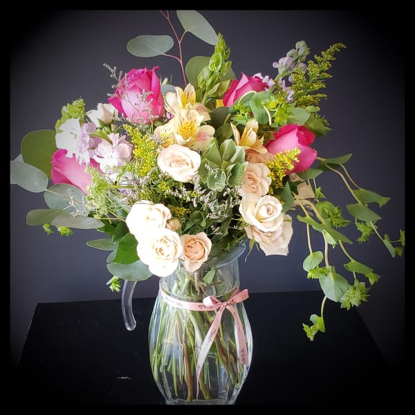 Mixed bouquet of pink and cream roses in a clear glass pitcher vase
