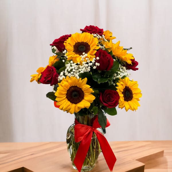 Bouquet of red roses and yellow sunflowers in a glass vase with a red ribbon