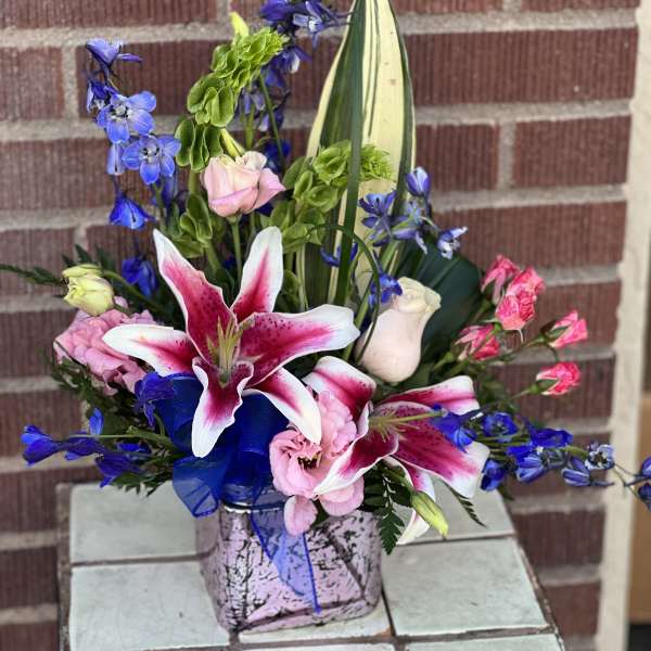 Pink and white lilies with blue flowers in a square vase