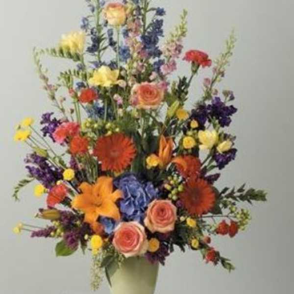 Tall mixed bouquet in a pale vase with roses, lilies, and blue flowers
