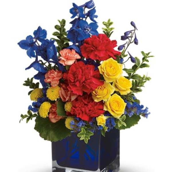Bright mixed bouquet in a square glass vase with blue, red, and yellow flowers