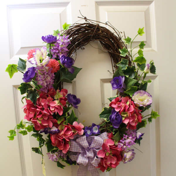Floral wreath with pink and purple flowers and a plaid bow on a door