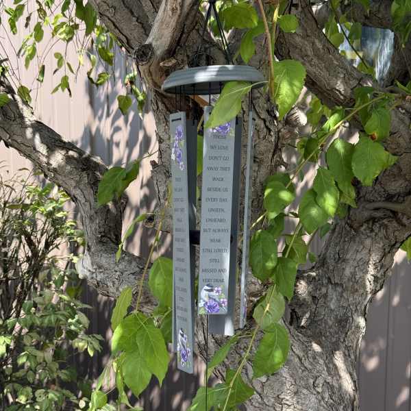 Hanging memorial wind chime with purple floral accents on a tree